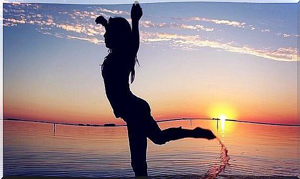 Woman in silhouette dancing in the sand by the water before sunset.