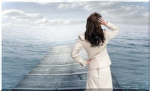 A woman is standing on a bridge and looking out to sea.