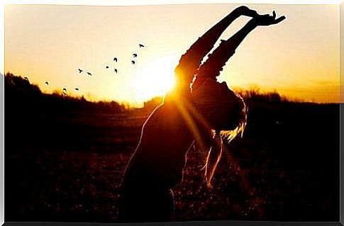 A woman is stretching in the sunset. 