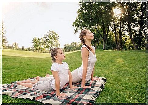 A mother and her child are in the park doing yoga on a blanket.