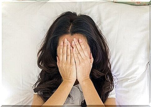 A woman is stressed out in bed with her hands in front of her face.