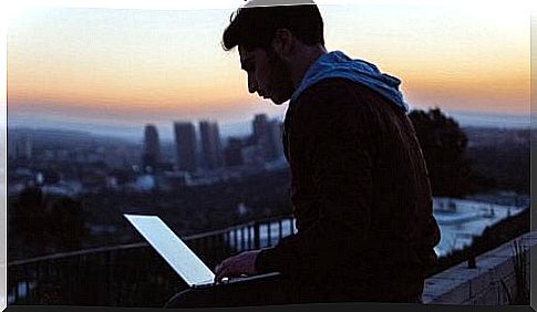 A man is sitting on a roof with his laptop.