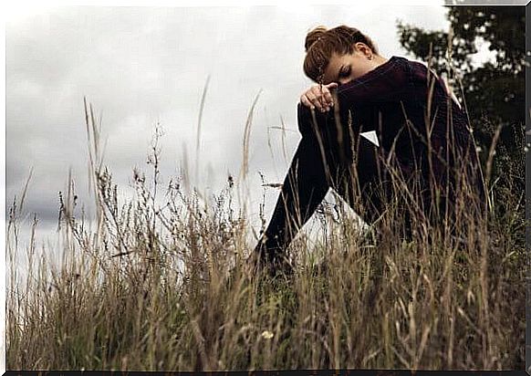 A young woman sits dejected on a bank. 