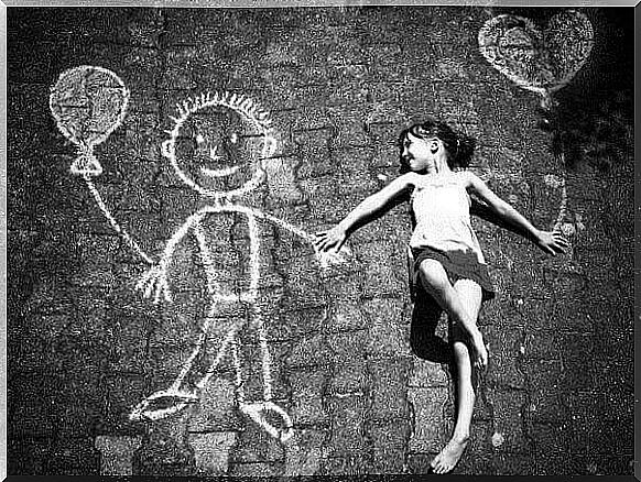 A girl lies on the floor and holds hands with a drawn chalk man.