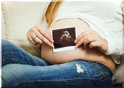 A pregnant woman holds the photo of her ultrasound in front of her stomach. 