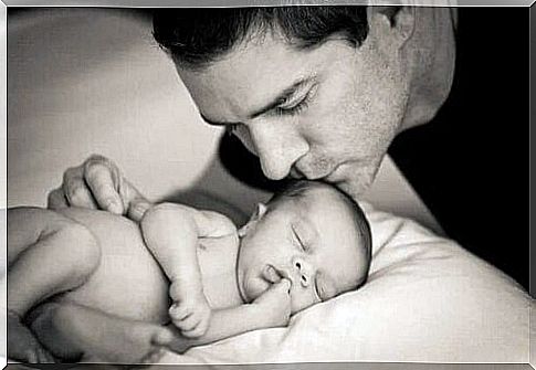 A young father kisses his baby who is lying in bed and sleeping.