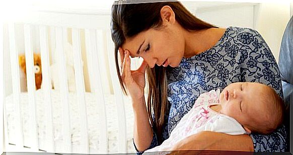 A young mother holds her baby in her arms while holding her forehead with one hand. 