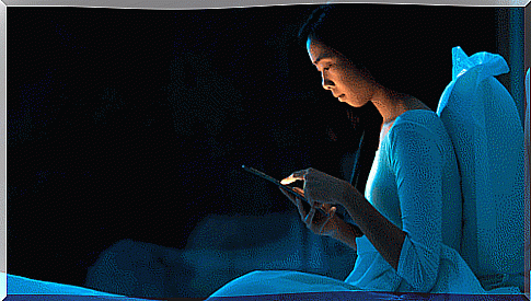 A young woman is typing on her cell phone in bed at night.