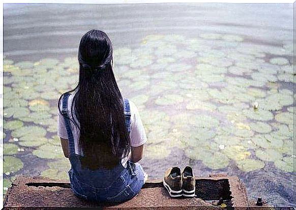 A girl is sitting on a jetty by the lily pond.