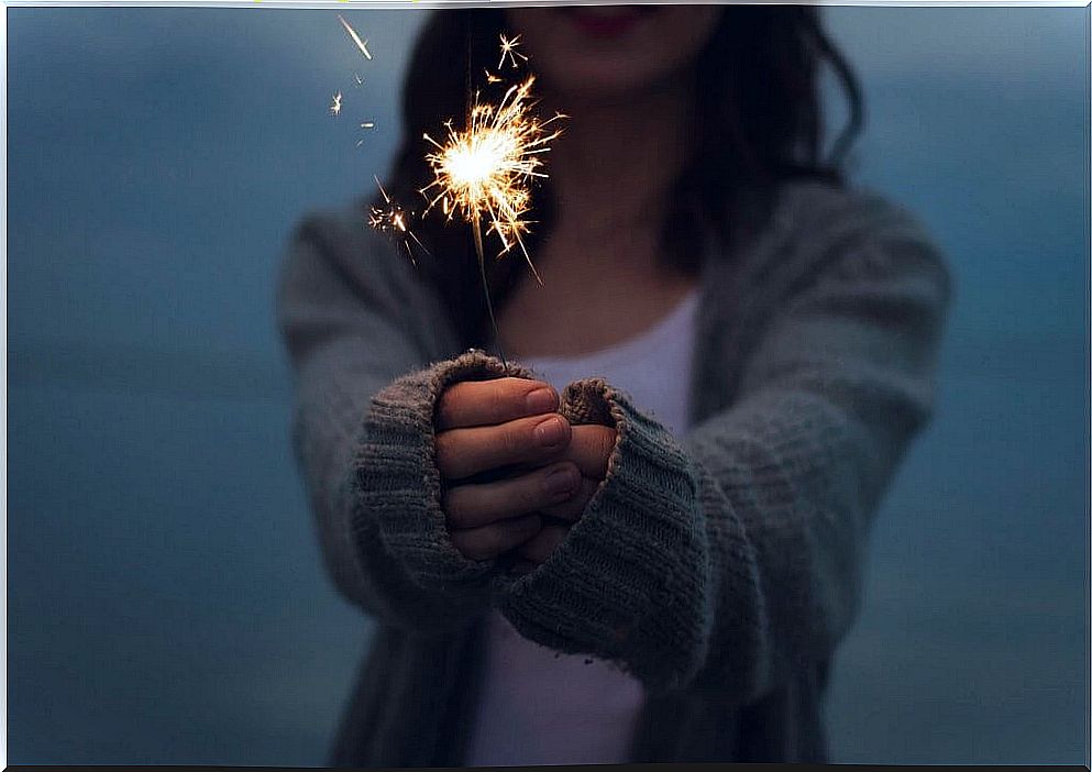 Woman holds out sparkler with both hands in front of her 